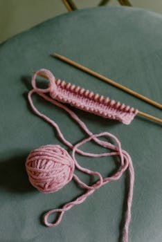 Pink yarn and knitting needles on green background, perfect for crafts and knitting themes.