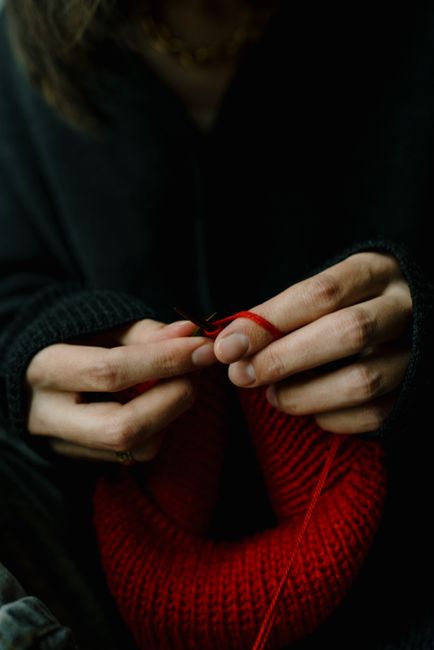 A detail shot of hands knitting with vibrant red yarn, showcasing craftsmanship.