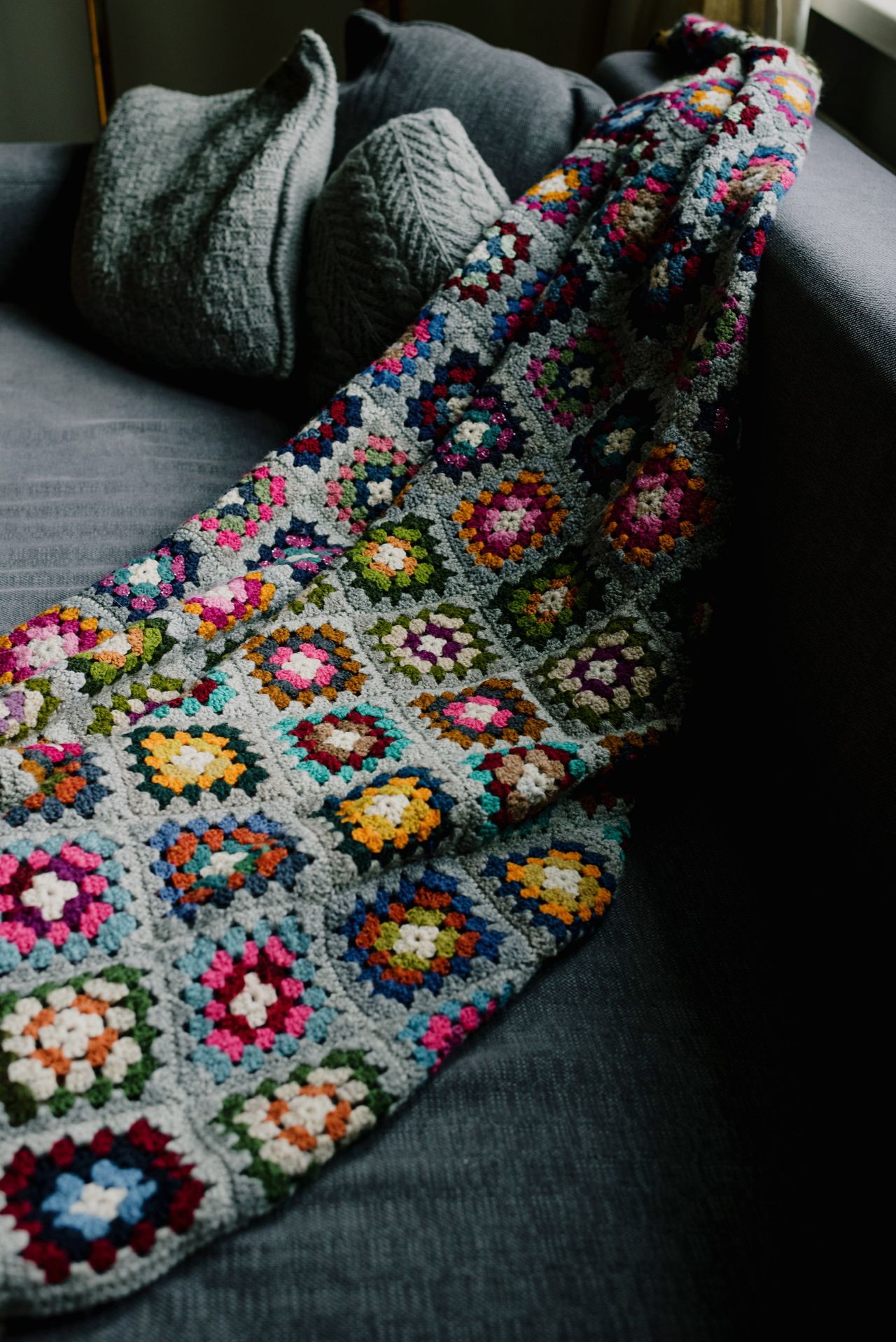 Colorful crocheted throw blanket draped over a gray sofa