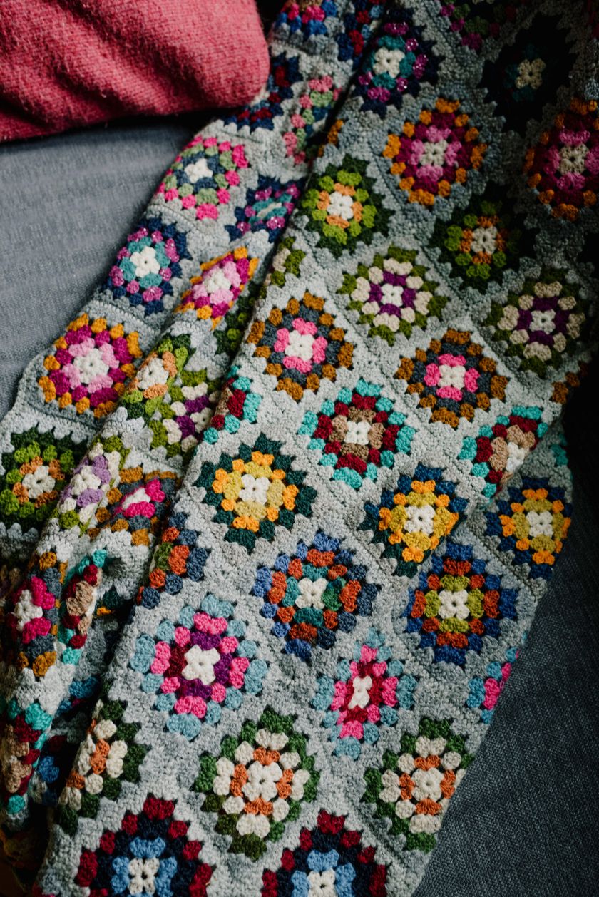 Close-up of a crocheted cloth, square openwork motifs in coloured yarn joined row by row.