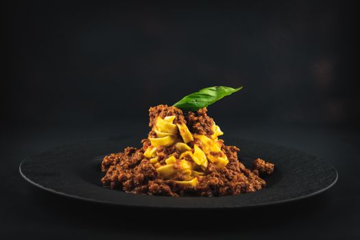 Tasty spaghetti bolognese beautifully presented on a black plate with a dark background.