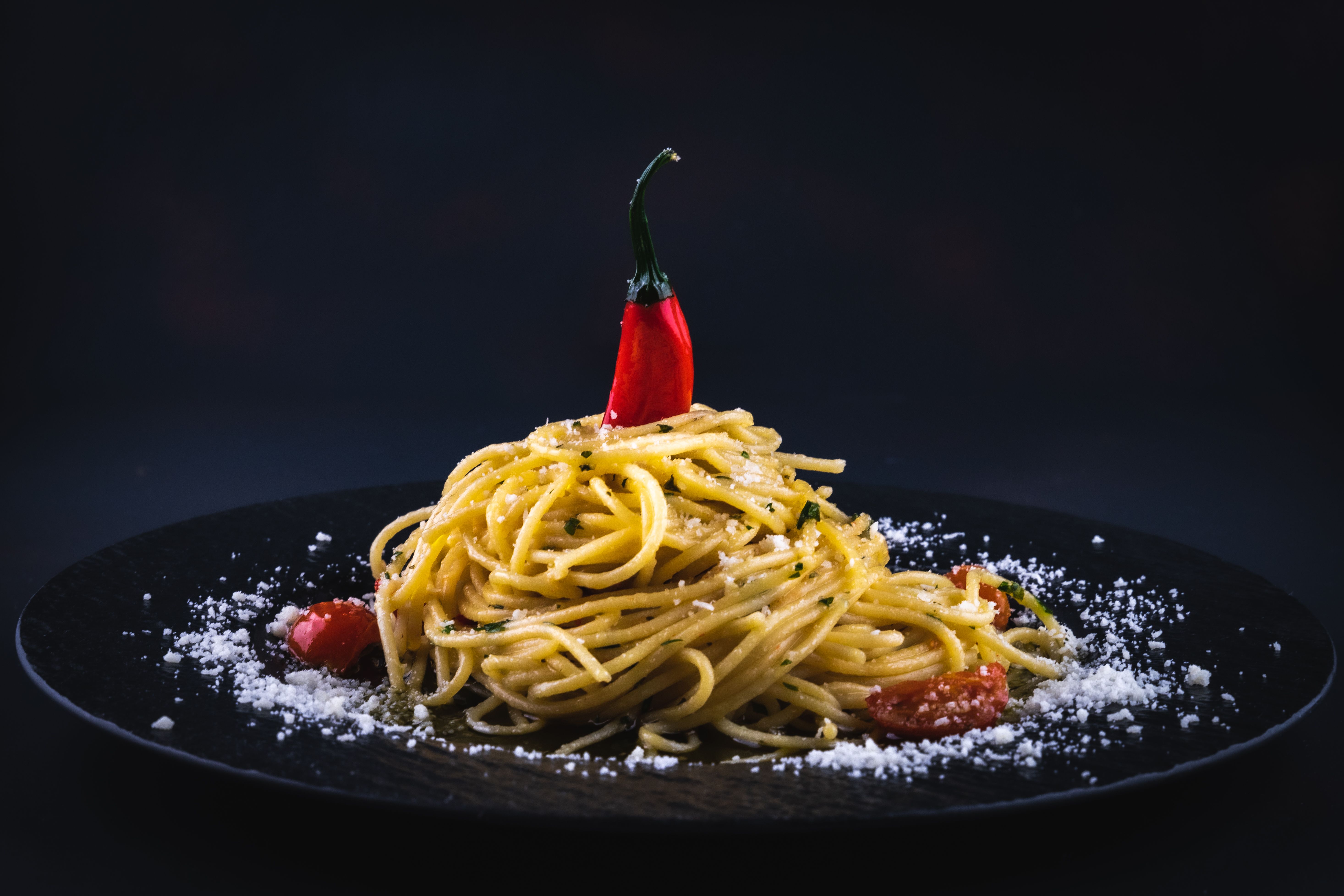 A beautifully styled plate of spaghetti with chili pepper on a black dish, garnished with 