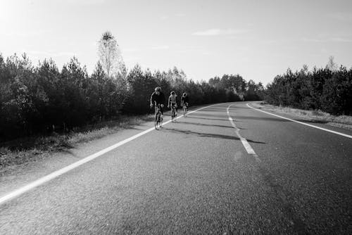 Grayscale Photo of Three People Biking on the Road