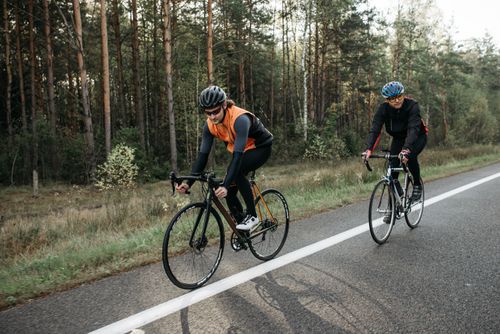 Free Two cyclists enjoying a ride through a scenic forest road, showcasing active lifestyle and outdoor recreation. Stock Photo