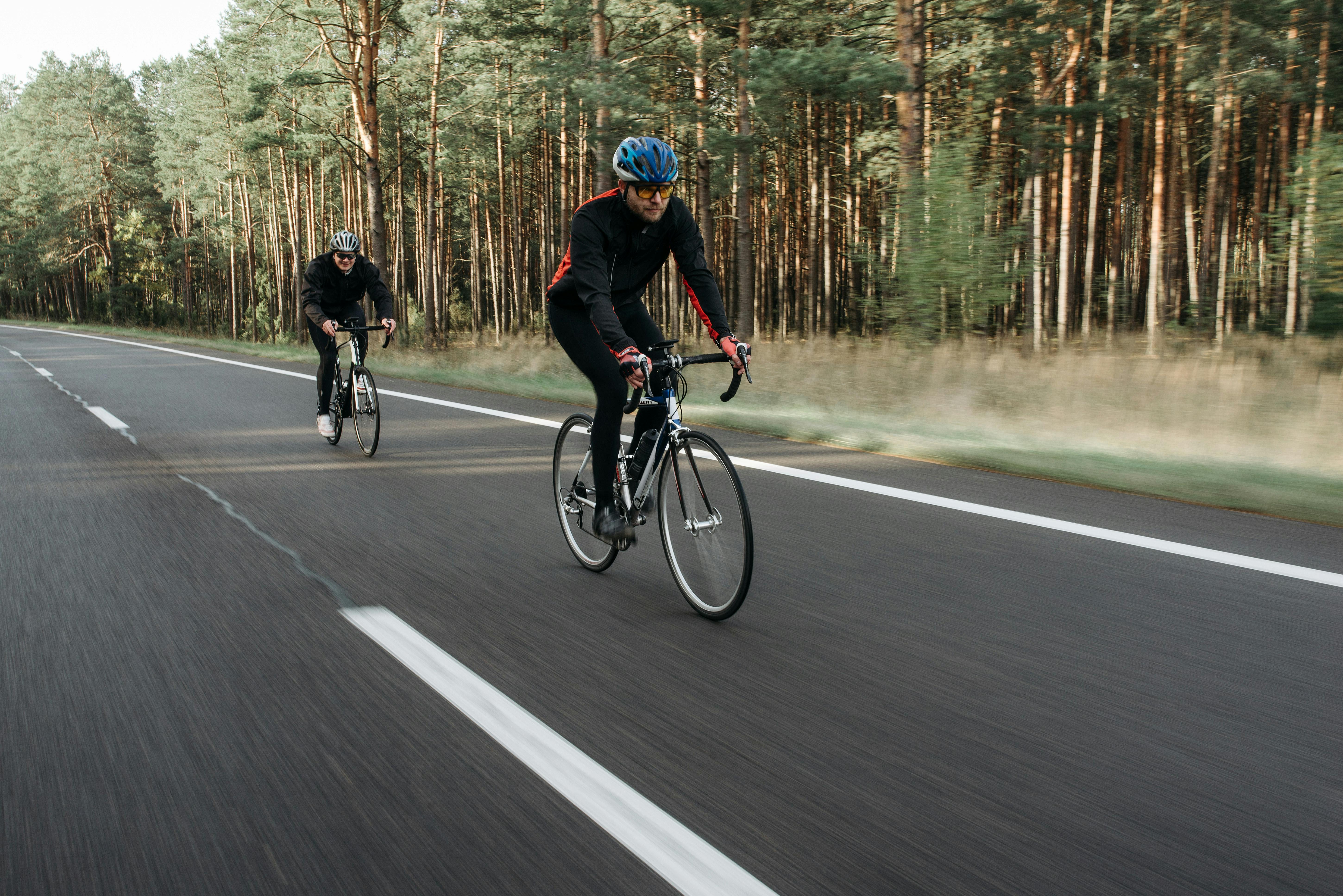 Two cyclists enjoying a refreshing ride on a forest road, showcasing active outdoor recreation.