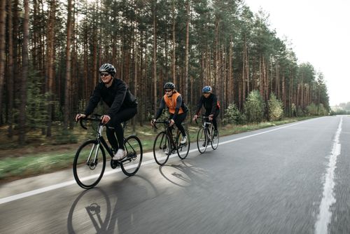 Free Three cyclists enjoying a ride on a road through a scenic forest landscape. Stock Photo