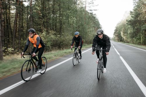 Free Group of cyclists in activewear biking on a forested road, enjoying outdoor recreation. Stock Photo