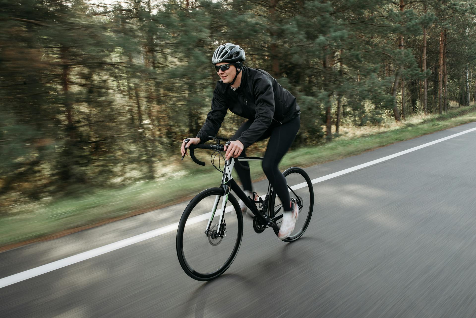 Man cycling on forest road in exercise gear, showcasing speed and determination.