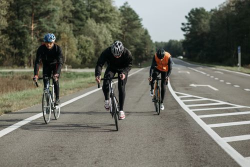 Free Three cyclists in activewear riding on a scenic road surrounded by nature during the day. Stock Photo