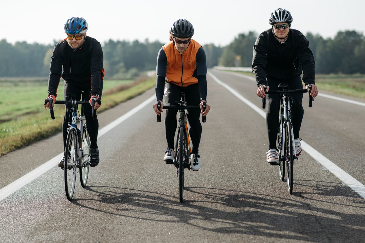 Drie wielrenners in winterjas en gilet rijden naast elkaar op een koude herfstweg