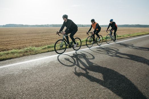 Three cyclists enjoy a leisurely ride on a rural road surrounded by fields