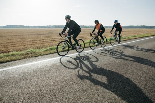 Free Three cyclists enjoy a leisurely ride on a rural road surrounded by fields Stock Photo