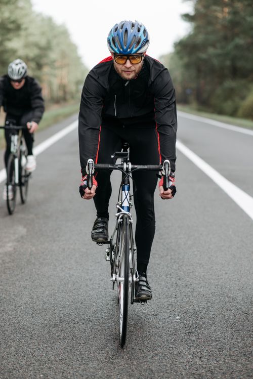 Free Two cyclists riding on a quiet road in activewear, perfect for fitness enthusiasts. Stock Photo