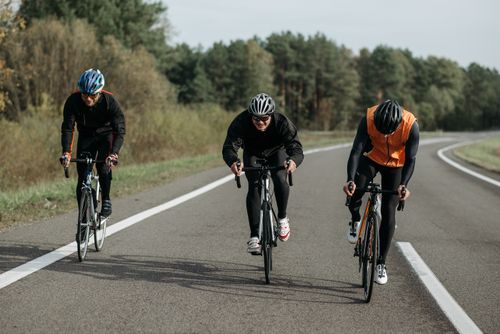 Free Three cyclists riding on a country road, showcasing fitness and outdoor activity. Stock Photo