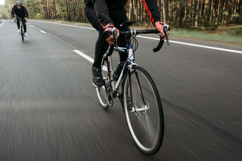 Cyclists racing on an open road surrounded by nature, showcasing speed.