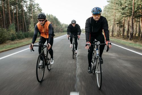 Free Three cyclists enjoying a ride through a forest road, showcasing outdoor fitness and teamwork. Stock Photo