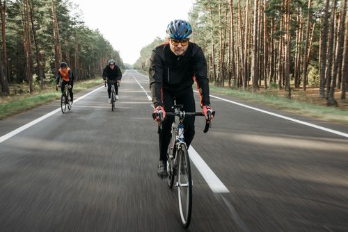 Free Group of cyclists riding through a forest on a quiet road during the day. Stock Photo