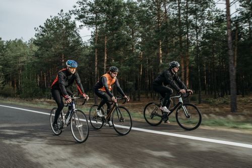 Free Group of cyclists riding on a road beside a forest, showcasing the thrill of outdoor biking. Stock Photo