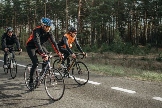 Three cyclists riding on a forest road, showcasing speed and fitness in casual sportswear.