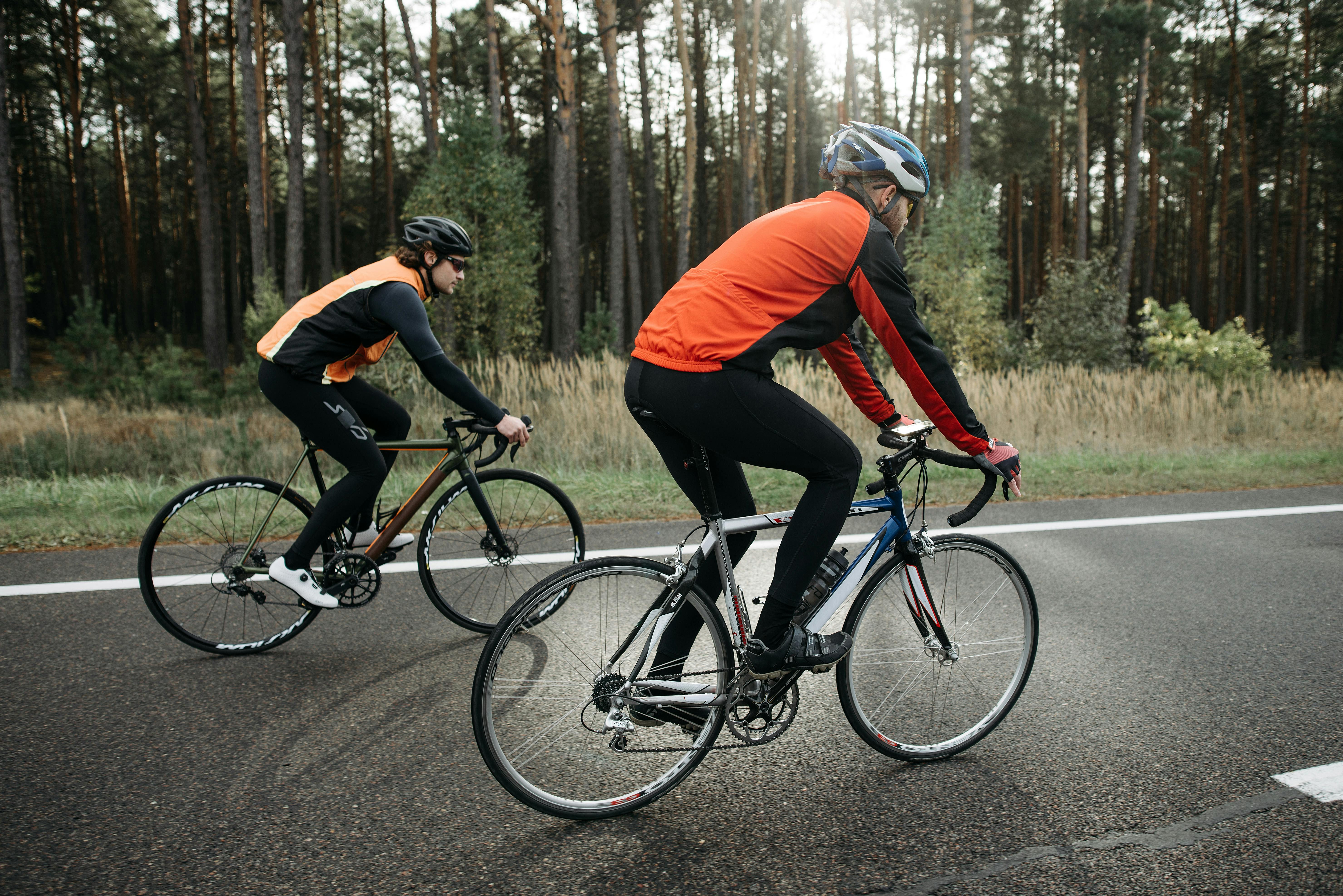 Two cyclists in vibrant gear biking along a forest road, enjoying a leisurely ride.