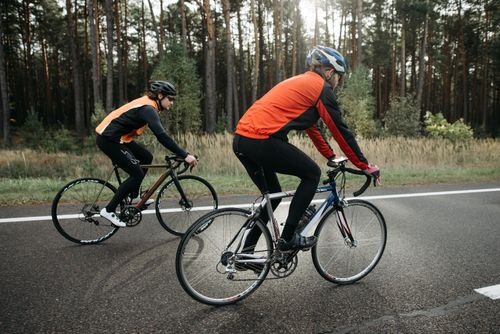 Free Two cyclists in vibrant gear biking along a forest road, enjoying a leisurely ride. Stock Photo