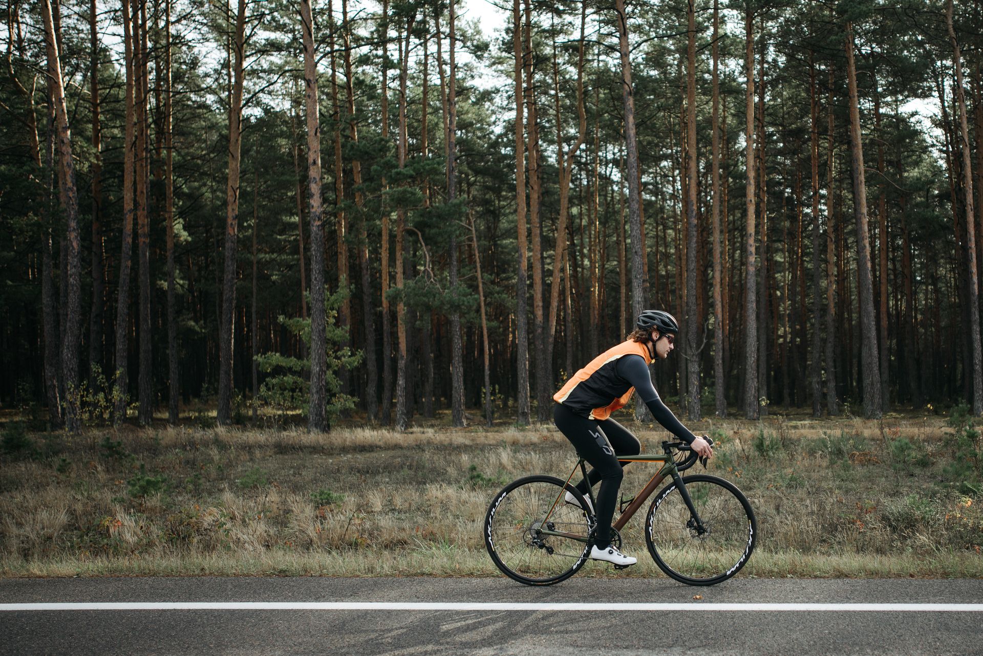 A cyclist rides past a dense forest on a clear day, enjoying outdoor biking near trees.