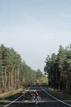Three cyclists taking a break on a forest-lined road, engaging in conversation.