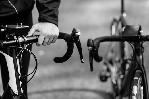 Black and white close-up of a cyclist gripping handlebars on a road bike outdoors.