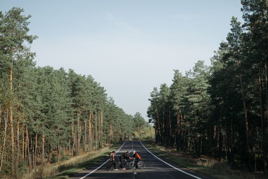 一群骑自行车的人在一条安静的乡村道路上休息，道路两旁森林茂密
