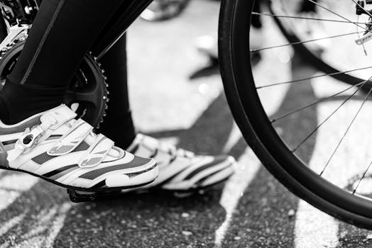 Black and white image showing a cyclist's feet with cleats on a bike pedal, capturing motion and detail.