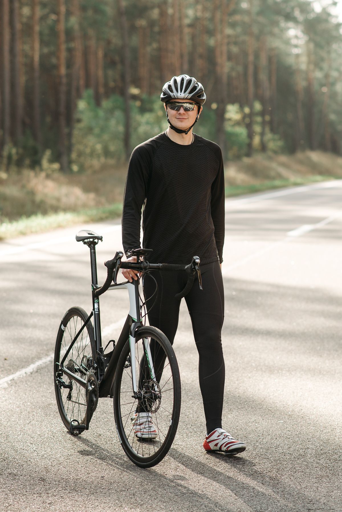 Cyclist wearing a helmet and sunglasses standing beside a bicycle on a forest road