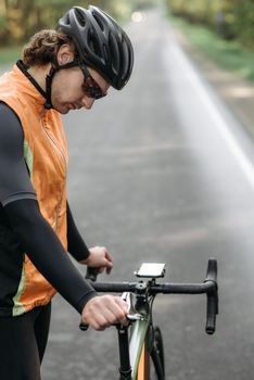 一名男子在安静的室外道路上调整着他的公路自行车，他戴着头盔