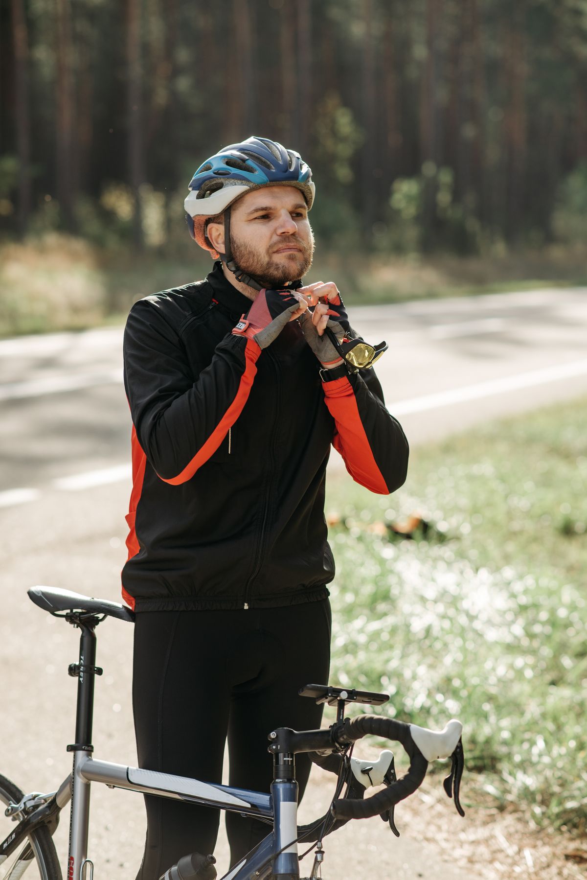 Cyclist adjusting his bicycle helmet while standing beside a road bicycle outdoors