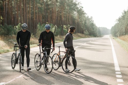 Free Three cyclists in activewear take a break on a scenic road surrounded by nature. Stock Photo