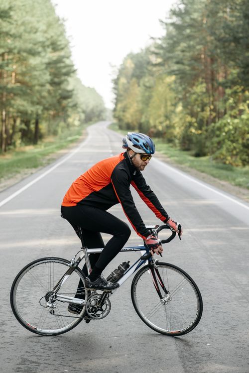 Free Male cyclist with helmet biking on a scenic road through forest during the day. Stock Photo