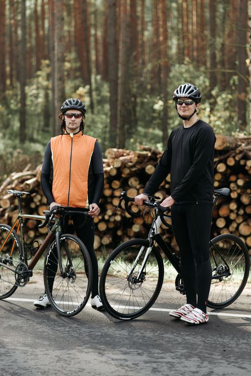 Free Two men with bicycles standing in front of wood logs in a forest setting, wearing helmets and activewear. Stock Photo