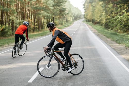 Free Two cyclists wearing helmets and sportswear biking on a forest road. Stock Photo
