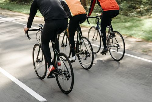 Free Group of cyclists riding on an outdoor path in bright sunlight, showcasing teamwork and fitness. Stock Photo