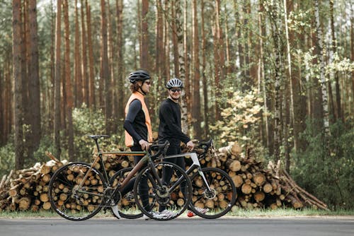 Two Men in Black Shirts Walking by the Road with Bicycles