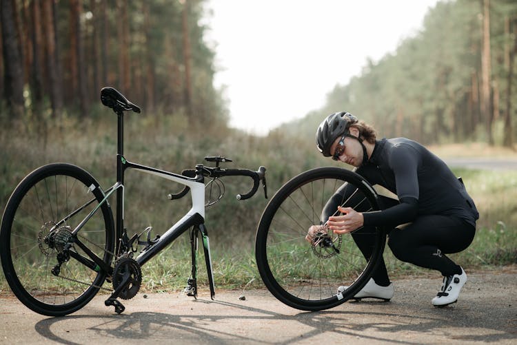 A Man In Black Long Sleeves Fixing His Bike