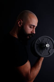 A bald man with a beard lifting a dumbbell against a dark background.
