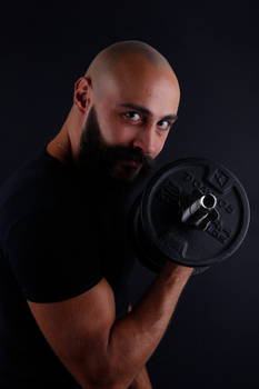 Bald man with a beard lifting a dumbbell, showcasing strength and fitness in a studio setting.