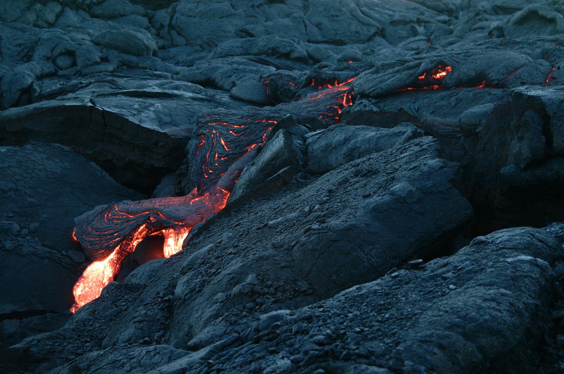 Captivating close-up of glowing molten lava flowing over solidified dark volcanic rocks.