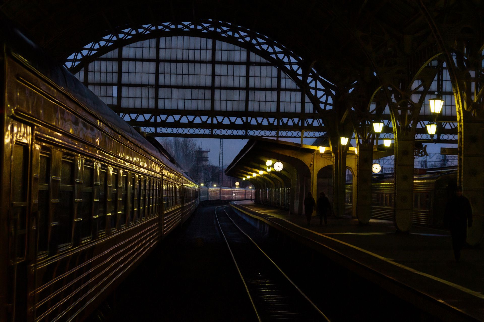 A classic urban railway station with arched design at twilight, featuring a train on the tracks and warm lighting.