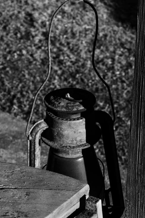 From above of black and white old shabby kerosene lamp hanging near wooden table in yard