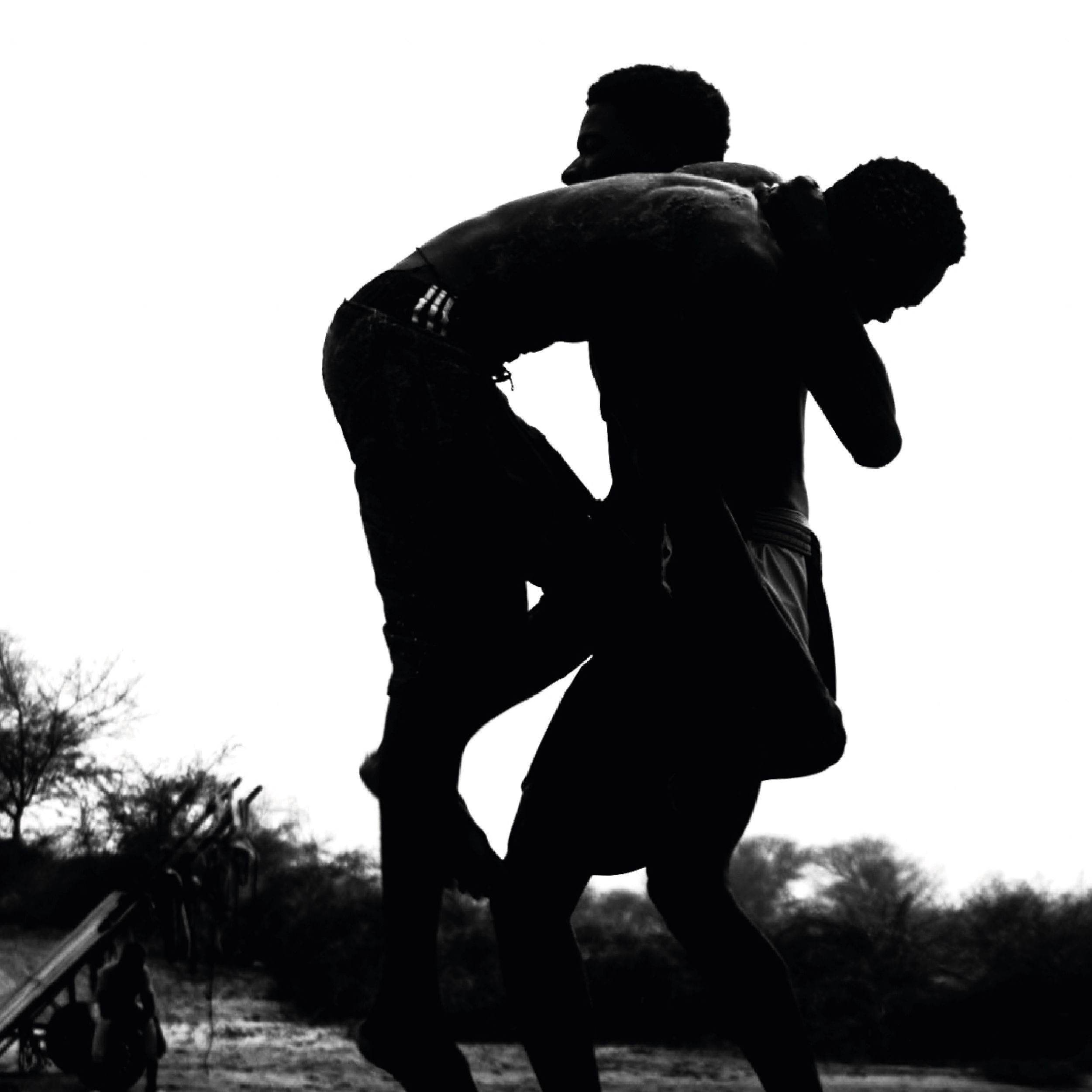Dynamic black and white silhouette of two men wrestling in an outdoor setting, showcasing strength.