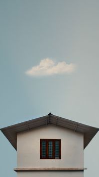 A single white house with a steep roof under a solitary cloud in a clear blue sky.