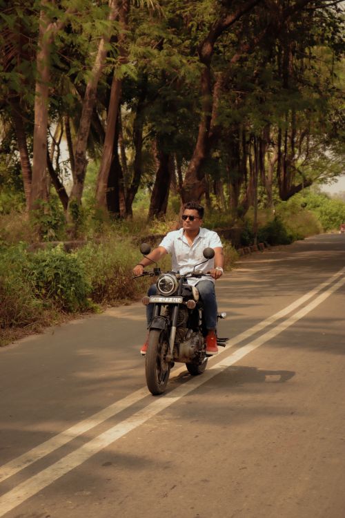 Free Full body of male biker in casual wear and sunglasses riding motorcycle on asphalt road along tall green trees in countryside Stock Photo