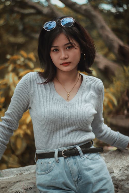 Free Portrait of a fashionable young woman wearing a gray sweater and sunglasses in an outdoor setting. Stock Photo