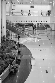 Grayscale image of a spacious modern interior with people walking and an escalator.
